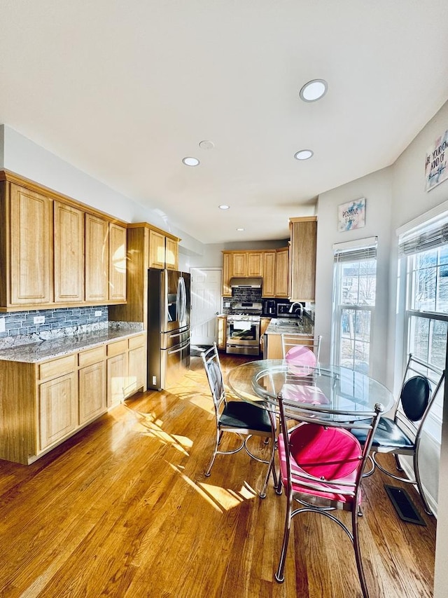 kitchen featuring sink, backsplash, stainless steel appliances, light stone countertops, and light wood-type flooring