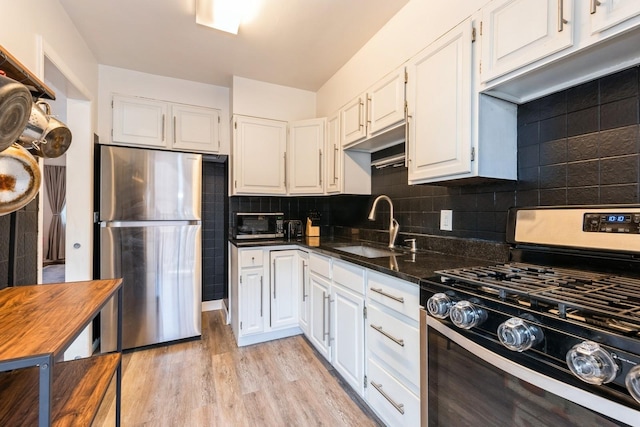 kitchen featuring sink, light hardwood / wood-style flooring, appliances with stainless steel finishes, dark stone countertops, and white cabinets