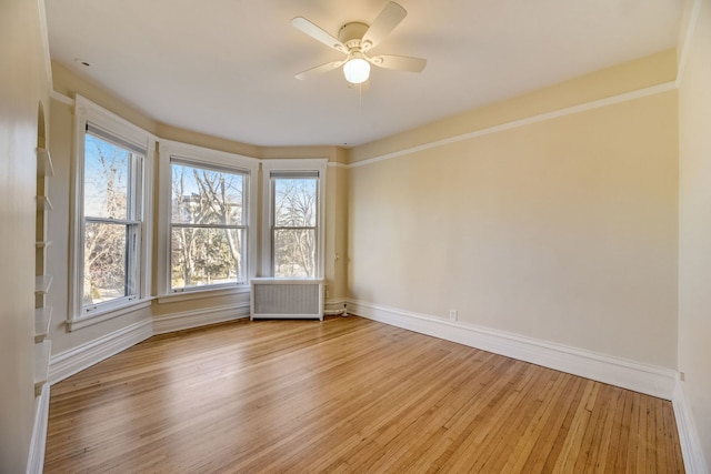 unfurnished room with ceiling fan, radiator, and light wood-type flooring