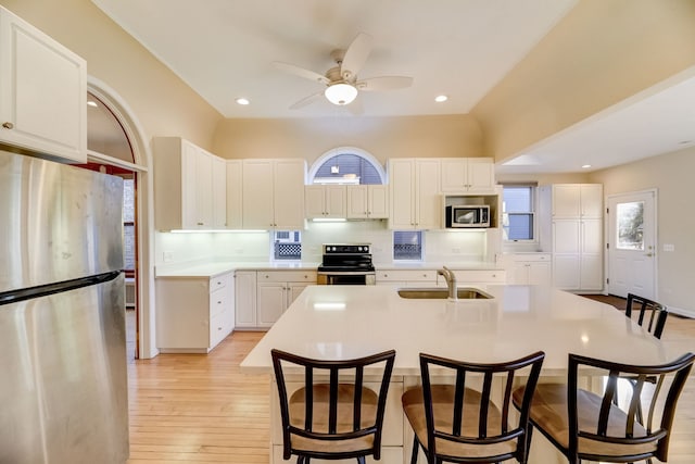 kitchen featuring appliances with stainless steel finishes, sink, white cabinets, decorative backsplash, and a center island with sink