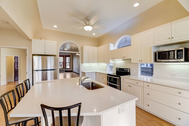 kitchen with sink, a center island with sink, a kitchen breakfast bar, stainless steel appliances, and decorative backsplash