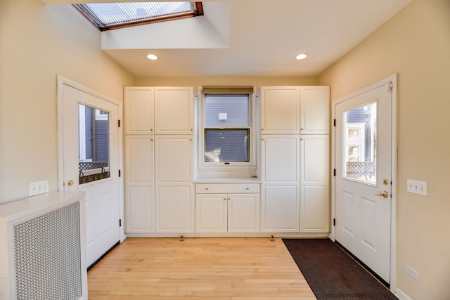 kitchen with radiator heating unit, white cabinets, light wood-type flooring, and a skylight