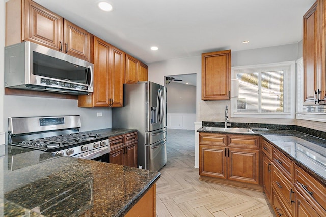 kitchen featuring stainless steel appliances, light parquet flooring, sink, and dark stone counters