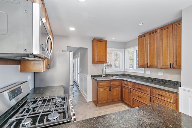 kitchen with sink, light parquet floors, stainless steel appliances, decorative backsplash, and dark stone counters