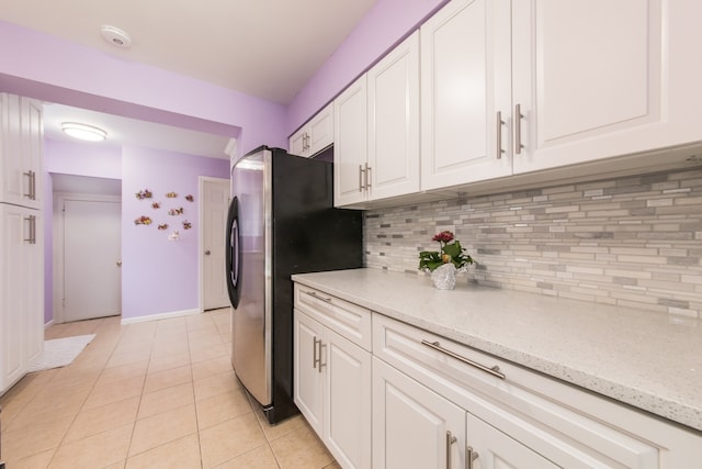 kitchen with tasteful backsplash, light stone countertops, white cabinets, stainless steel fridge, and light tile patterned floors