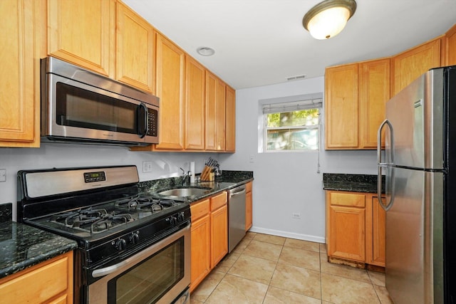 kitchen with appliances with stainless steel finishes, sink, light tile patterned floors, and dark stone counters