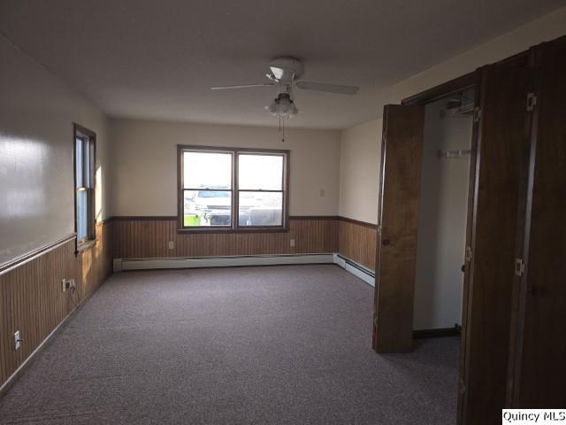 carpeted spare room with a baseboard radiator, ceiling fan, and wood walls