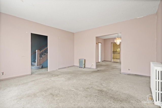 unfurnished room with radiator, light colored carpet, a textured ceiling, and a chandelier