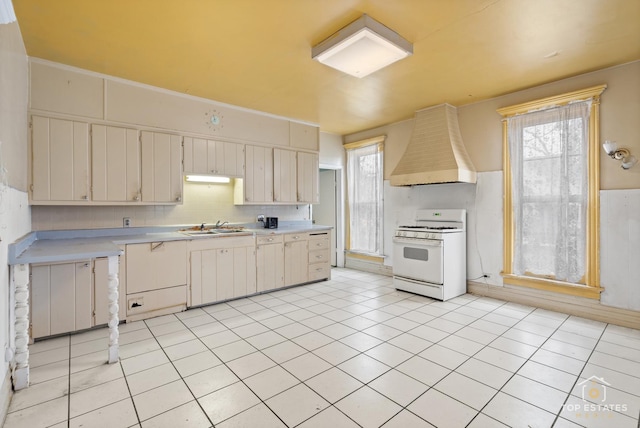 kitchen with sink, white gas stove, light tile patterned floors, custom range hood, and backsplash