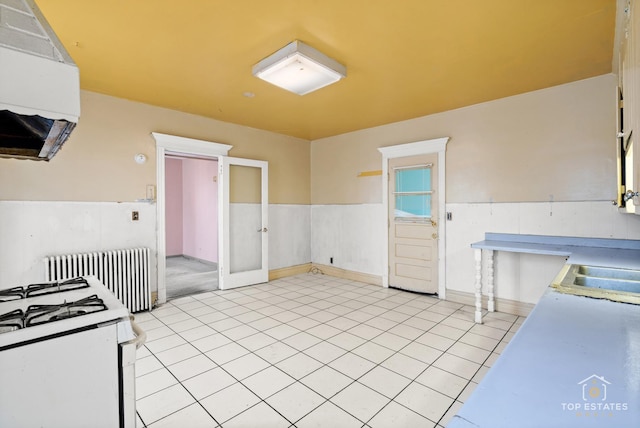 kitchen featuring light tile patterned flooring, sink, extractor fan, radiator heating unit, and white gas range oven