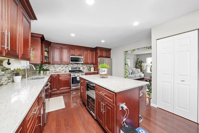 kitchen with sink, appliances with stainless steel finishes, light stone countertops, a kitchen island, and beverage cooler