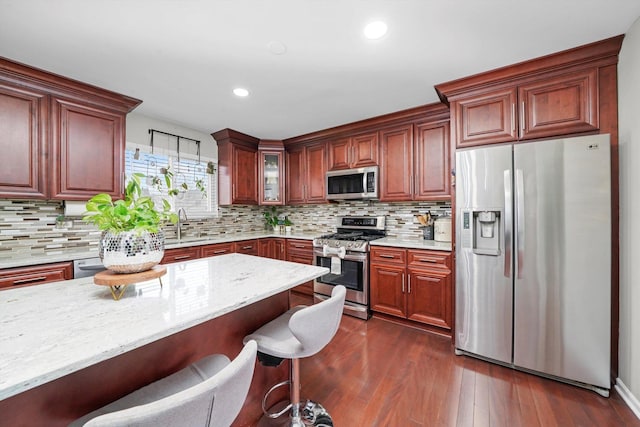 kitchen with stainless steel appliances, dark hardwood / wood-style flooring, a kitchen breakfast bar, and decorative backsplash