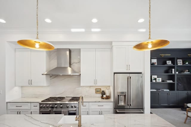 kitchen with high end appliances, white cabinets, wall chimney exhaust hood, and pendant lighting