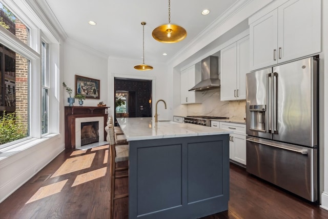 kitchen featuring wall chimney range hood, white cabinetry, hanging light fixtures, high quality fridge, and light stone countertops