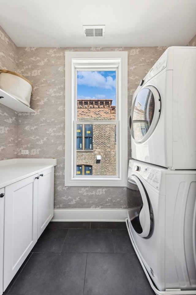 laundry room with cabinets, stacked washer / dryer, and dark tile patterned floors