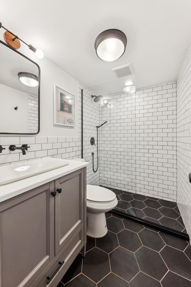 bathroom with tile patterned flooring, vanity, tiled shower, and tile walls