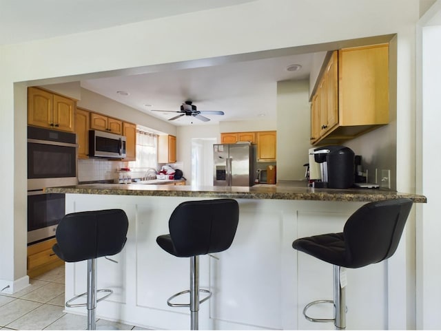 kitchen featuring appliances with stainless steel finishes, a breakfast bar, kitchen peninsula, and light tile patterned floors