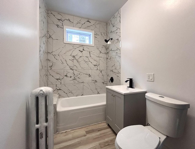 full bathroom with tiled shower / bath, radiator, hardwood / wood-style floors, vanity, and toilet