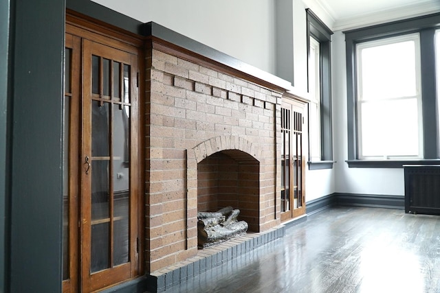 unfurnished living room with a brick fireplace, wood-type flooring, and ornamental molding