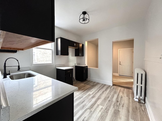 kitchen with sink, radiator heating unit, light stone counters, and light hardwood / wood-style floors