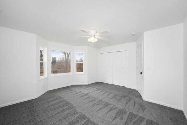 empty room featuring ceiling fan, a textured ceiling, and dark carpet