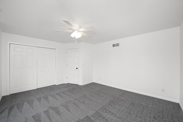 unfurnished bedroom featuring ceiling fan, dark carpet, a closet, and a textured ceiling