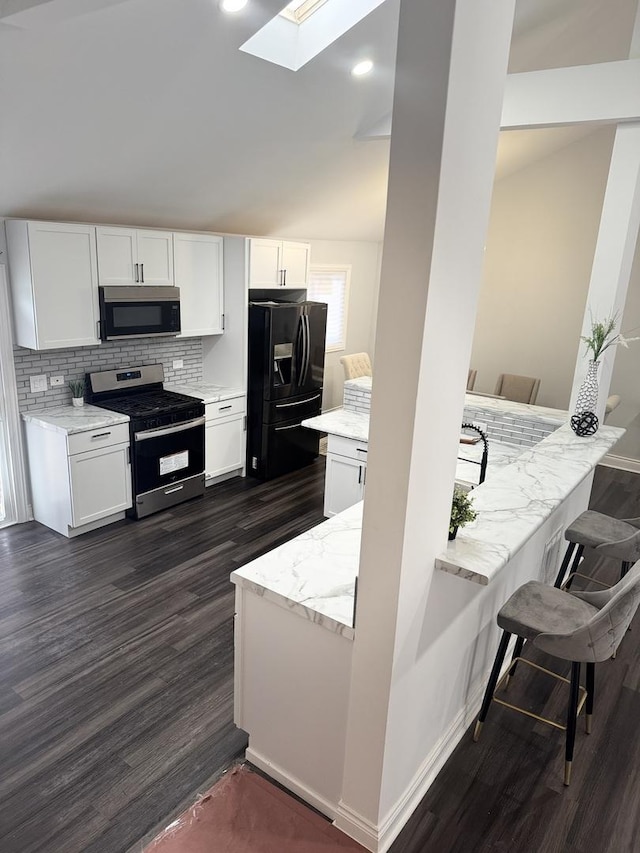 kitchen featuring white cabinetry, light stone counters, a skylight, appliances with stainless steel finishes, and decorative backsplash