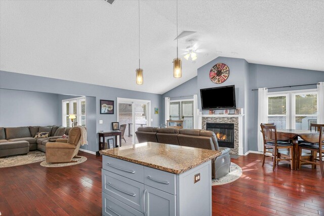 kitchen featuring decorative light fixtures, dark hardwood / wood-style flooring, a kitchen island, a fireplace, and light stone countertops