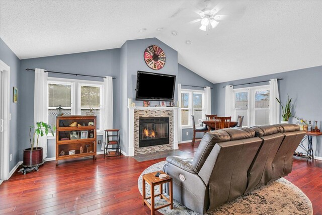 living room featuring dark wood-type flooring, ceiling fan, a textured ceiling, a tiled fireplace, and vaulted ceiling