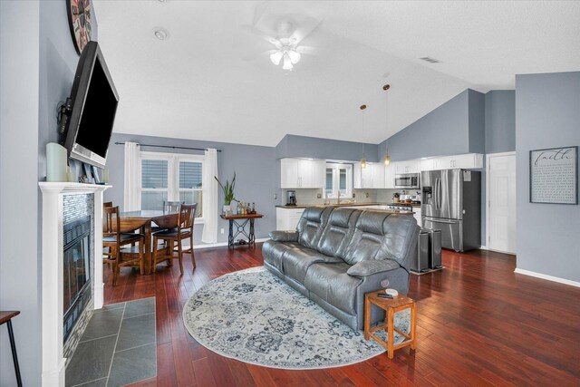 living room featuring a tile fireplace, high vaulted ceiling, sink, dark hardwood / wood-style flooring, and ceiling fan