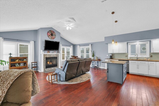 living room featuring lofted ceiling, sink, dark hardwood / wood-style floors, ceiling fan, and a fireplace
