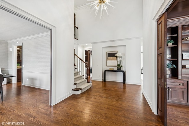 entryway featuring ornamental molding, dark hardwood / wood-style floors, a notable chandelier, and a towering ceiling