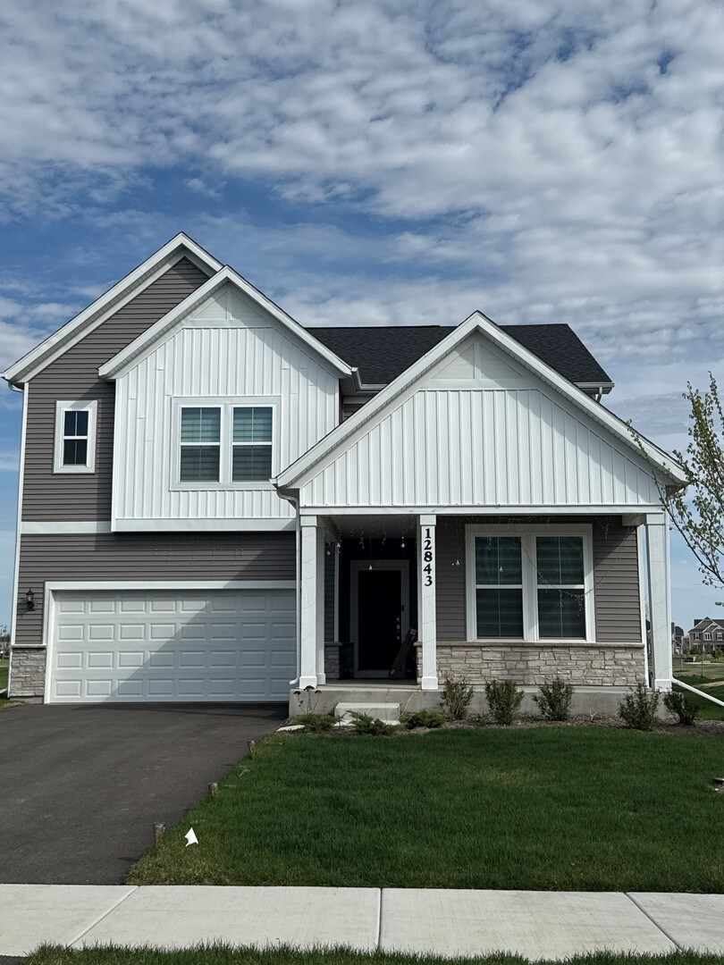 12929 S Beckham Dr, Plainfield, IL 60585 - view of front facade with board and batten siding, a porch, a garage, stone siding, and a front lawn