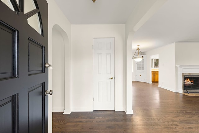 foyer entrance with baseboards, a fireplace, arched walkways, and dark wood-type flooring