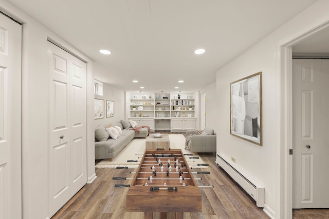 living room with built in shelves, recessed lighting, baseboard heating, and wood finished floors