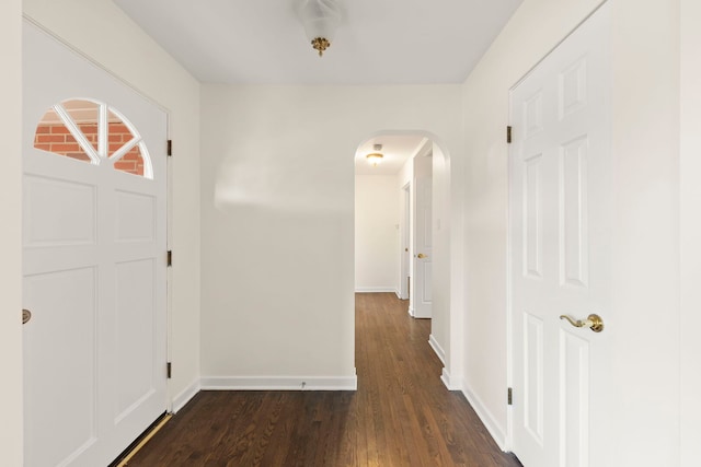 entryway with dark wood-type flooring, arched walkways, and baseboards