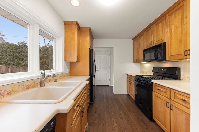 kitchen with dark wood finished floors, decorative backsplash, light countertops, black appliances, and a sink