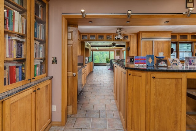 kitchen featuring paneled refrigerator, dark stone counters, and ceiling fan