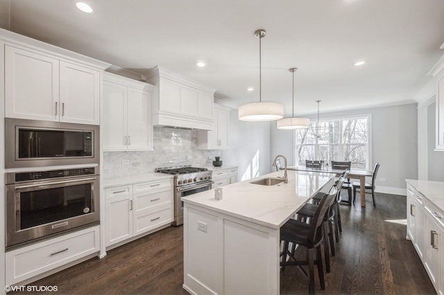 kitchen featuring pendant lighting, sink, white cabinetry, stainless steel appliances, and a center island with sink