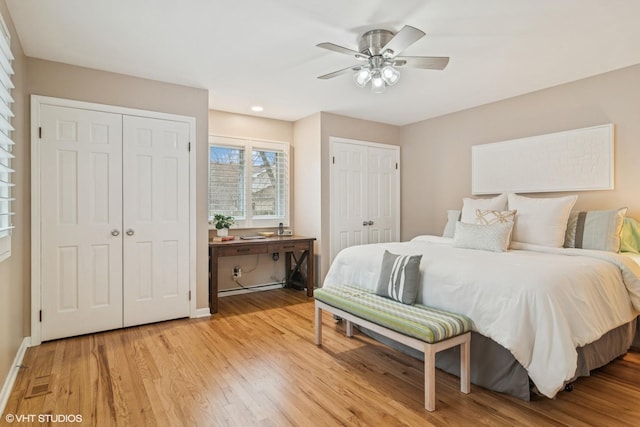 bedroom featuring light wood finished floors, a ceiling fan, baseboards, and multiple closets