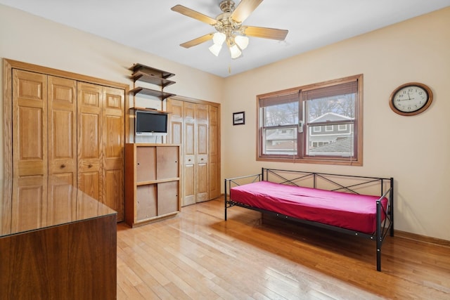 bedroom with ceiling fan, light hardwood / wood-style flooring, and multiple closets