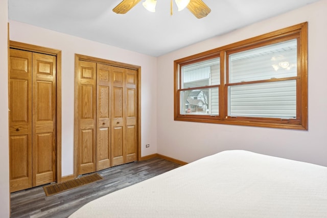 bedroom with multiple closets, dark hardwood / wood-style floors, and ceiling fan