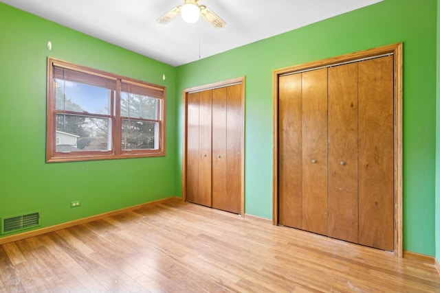 unfurnished bedroom featuring multiple closets, ceiling fan, and light hardwood / wood-style flooring