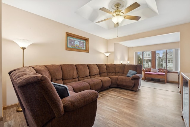 living room with a raised ceiling, ceiling fan, and light hardwood / wood-style flooring