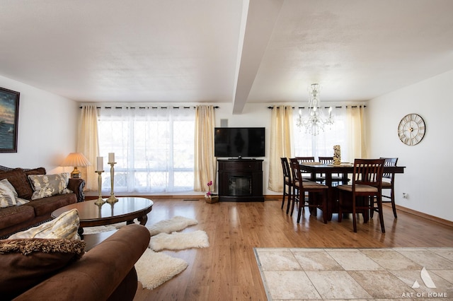 living room with beam ceiling, a healthy amount of sunlight, a chandelier, and light wood-type flooring