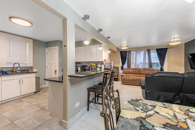 kitchen with a breakfast bar, sink, white cabinetry, tasteful backsplash, and pendant lighting