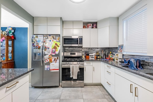 kitchen featuring stainless steel appliances, white cabinets, dark stone counters, and decorative backsplash