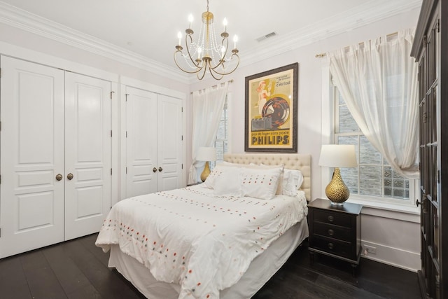 bedroom with crown molding, dark hardwood / wood-style floors, a chandelier, and two closets