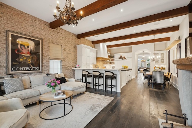 living room with dark hardwood / wood-style flooring, a notable chandelier, beam ceiling, and brick wall