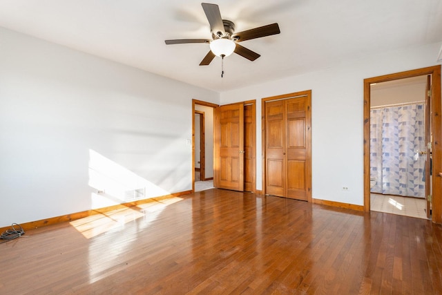 unfurnished bedroom with visible vents, baseboards, a ceiling fan, wood-type flooring, and multiple closets